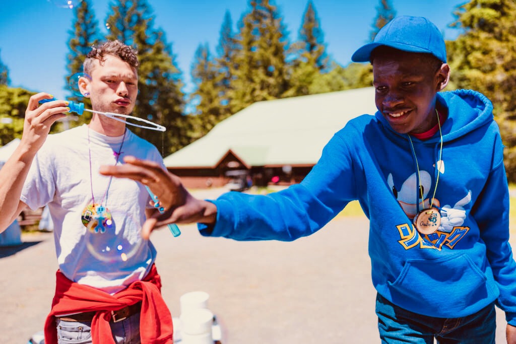 Counselor blowing bubbles, with camper trying to catch one.