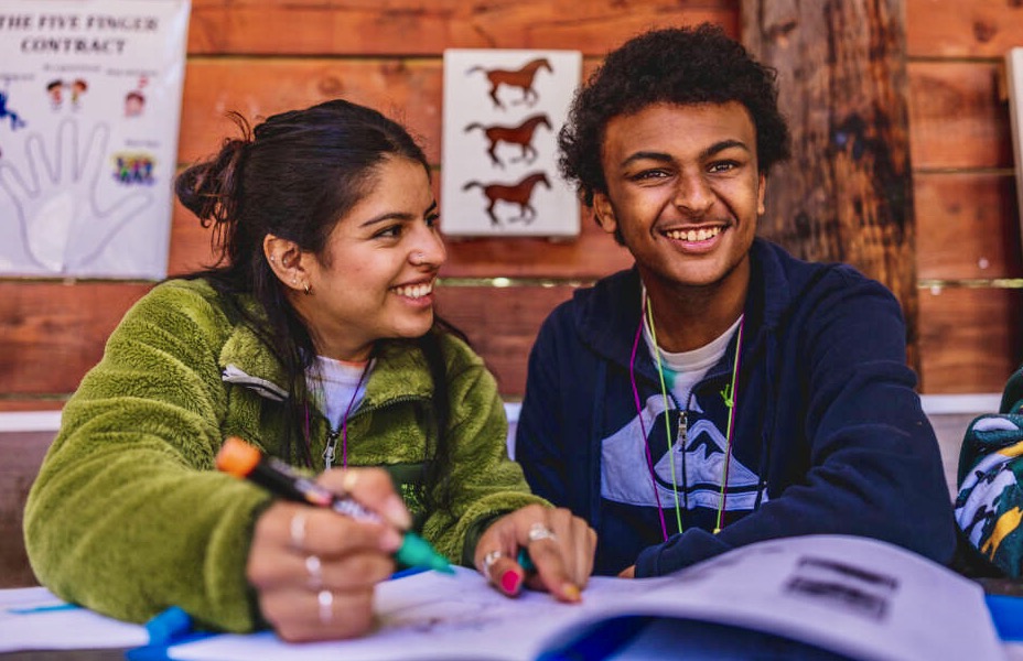 Smiling camper and counselor journaling together at the horse corral.