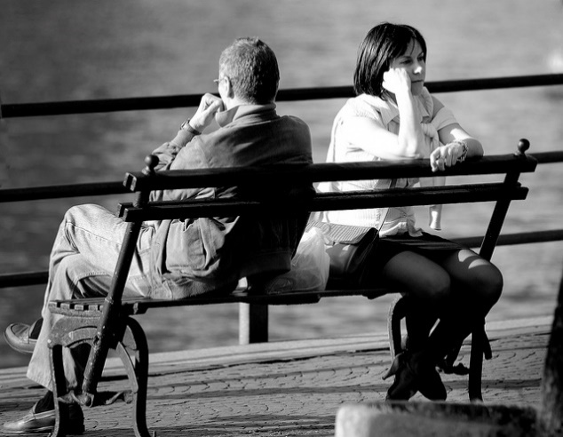 Photograph: Two people sitting on a park bench, facing away from each other in silent anger