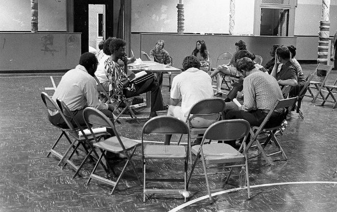 Photograph: a group of people sitting in folding chairs in a circle, having a conversation.
