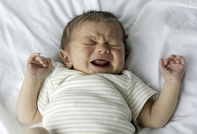 'a baby crying on a white blanket'