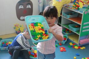 A young child holds a basket full of small multi-colored plastic shapes.